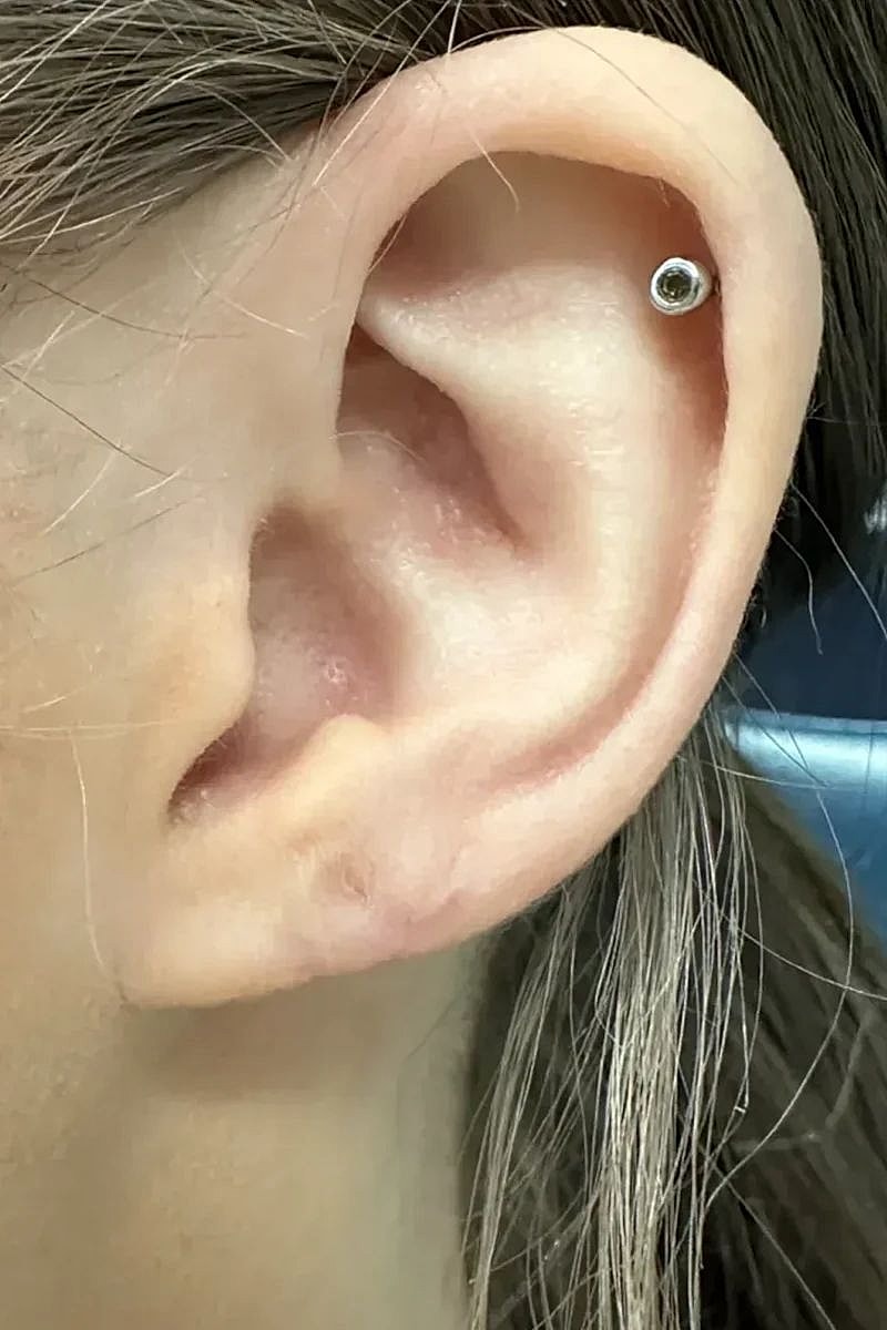 Ear with a decorative piercing and hair strands.