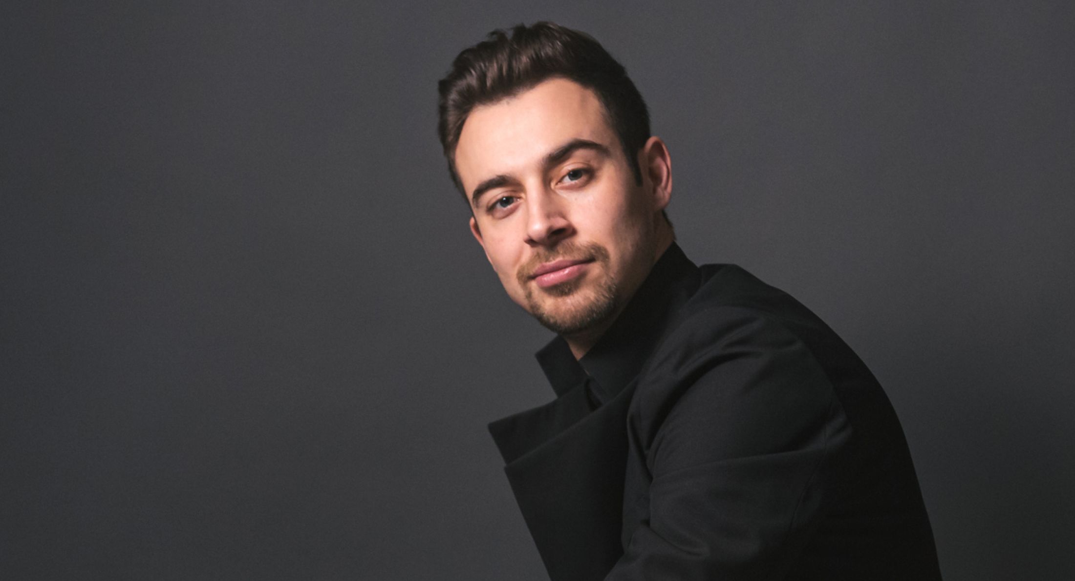 Man in black outfit posing against dark background.