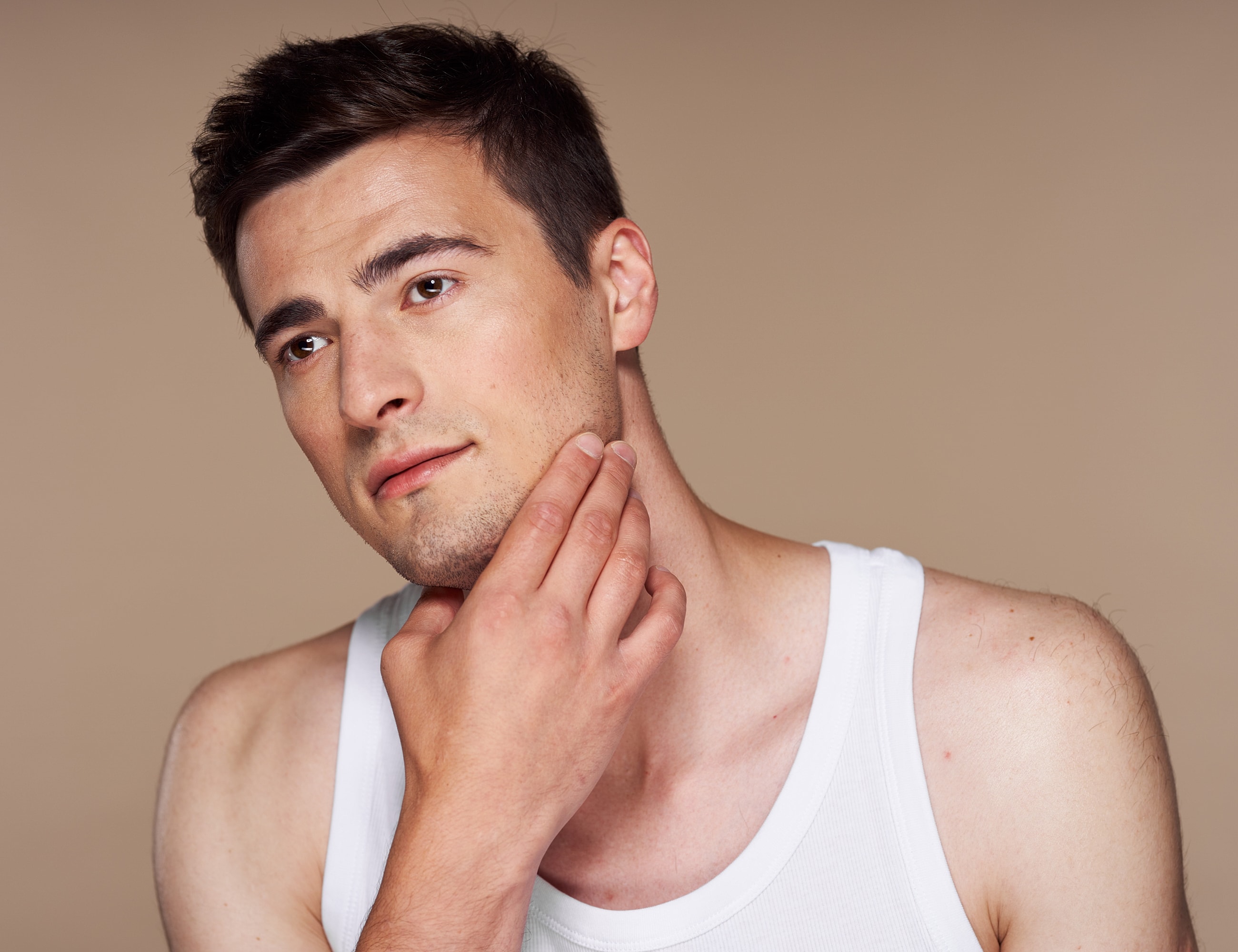 Young man touching his chin, neutral background.