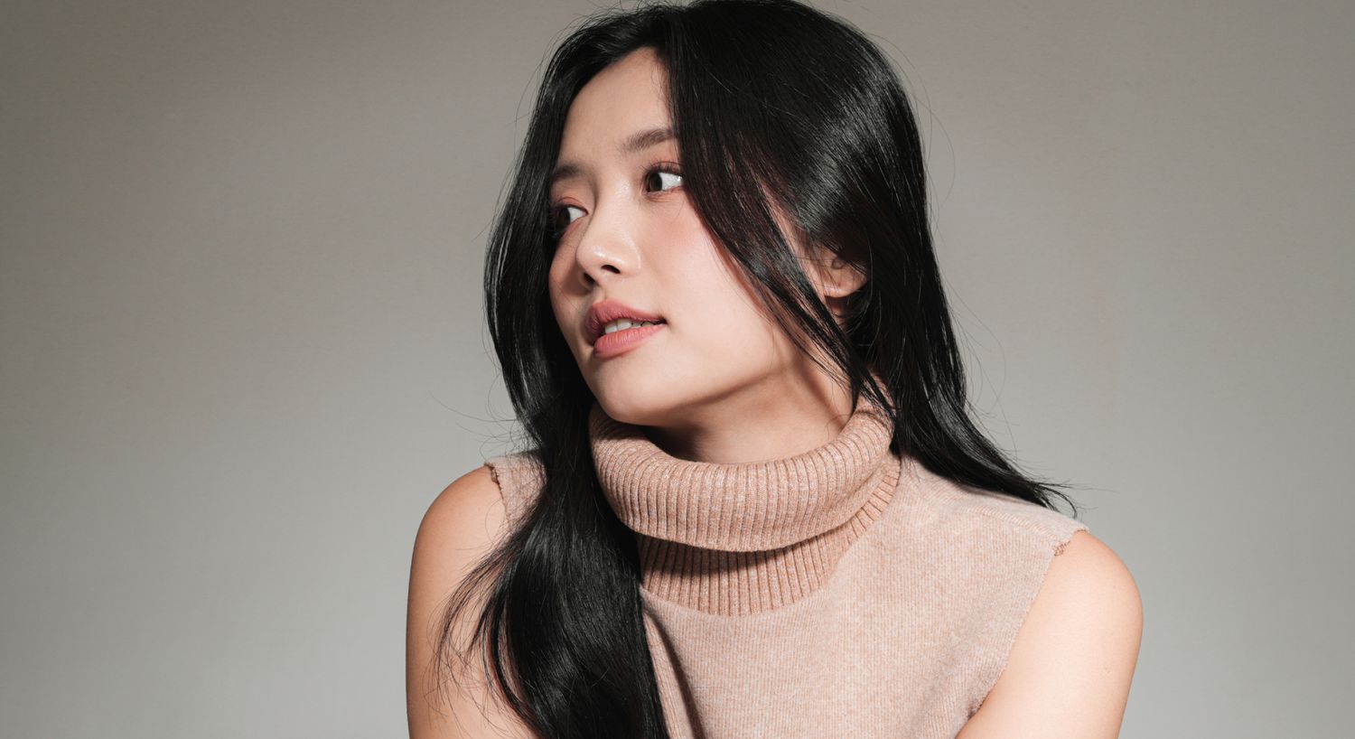 Model with long black hair in turtleneck sweater.