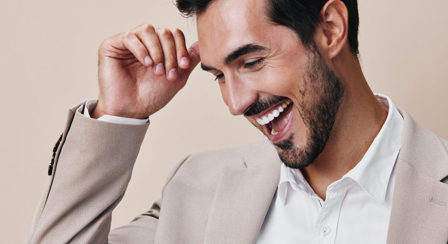 Smiling man in a light suit, joyful expression.